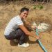 Ragazza sorridente accucciata a terra com pompa d'acqua in mano in terreno arido - Agnese Ferrara Servizio Civile Senegal