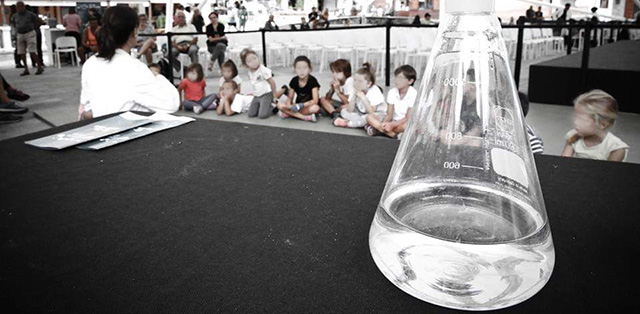 Tavolo con in primo piano ampolla di vetro per esperimenti, sfondo di bambini
