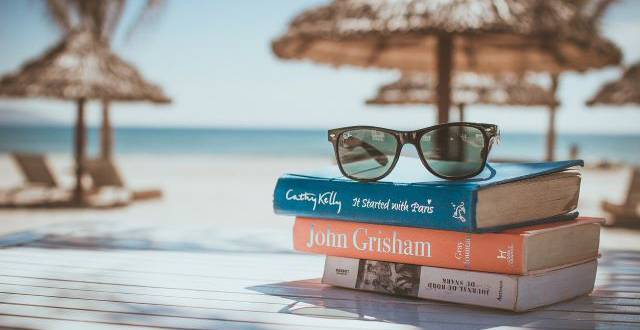 Pila di tre libri con occhiali da sole e sfondo ombrelloni