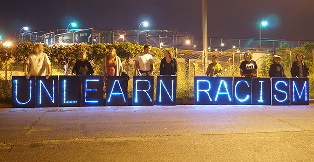 Persone con lettere luminose a comporre Unlearn racism - razzismo