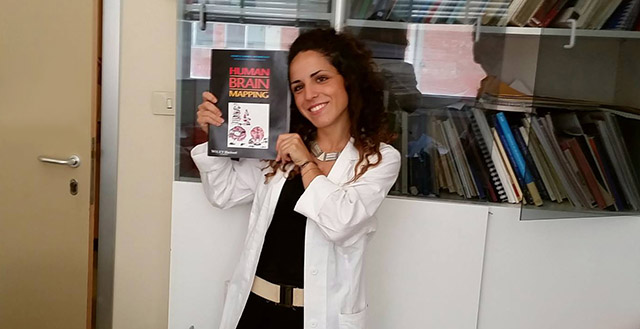Donna con camice bianco che sorride mostrando una rivista - Elisa Tatti ricercatrice
