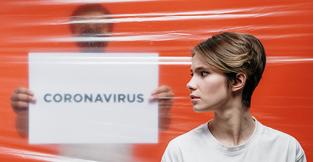 Ragazza di profilo davanti a telone trasparente con cartello Coronavirus
