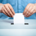 Mani che infilano foglio in urna elettorale - referendum